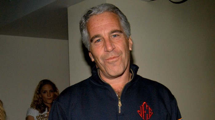 Jeffrey Epstein stands indoors at the launch of Radar Magazine, wearing a dark zip-up top with red initials.