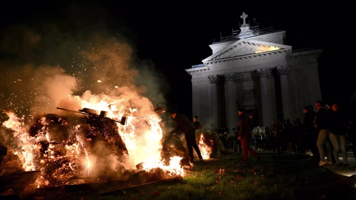 Protesters stand around a large fire, burning debris outside a neoclassical building at night during a farmers demonstration.