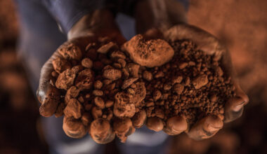 Hands holding a pile of reddish-brown crushed bauxite ore