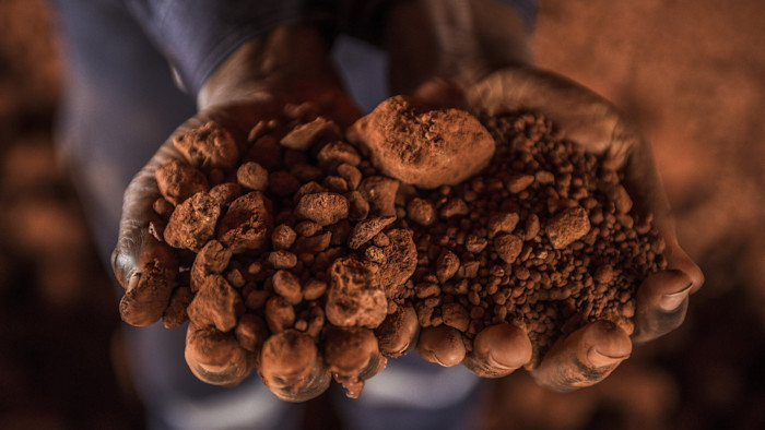 Hands holding a pile of reddish-brown crushed bauxite ore