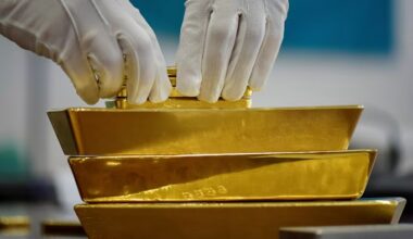 Gloved hands arranging gold bars stacked in a vault