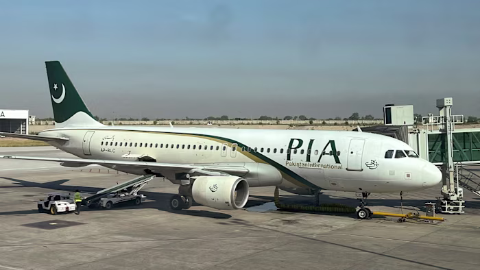 A Pakistan International Airlines passenger plane is parked at a gate, with ground crew working nearby at Islamabad International Airport.