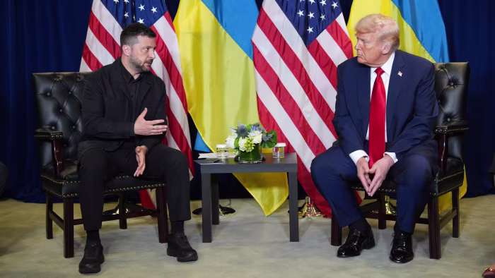 President Donald Trump and Ukrainian President Volodymyr Zelenskyy sit facing each other with flags behind them during a meeting.