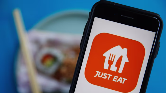 The Just Eat logo displayed on a smartphone screen, with blurred food and chopsticks in the background.