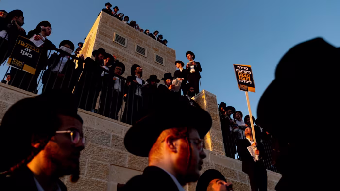 Ultra-Orthodox Jewish men stand on a building and hold protest signs during a large anti-draft rally in Jerusalem.