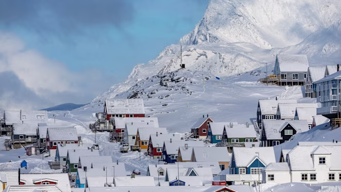 Snow-covered houses in Nuuk, Greenland, with Sermitsiaq Mountain rising in the background under a partly cloudy sky.