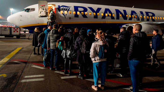 Passengers stand in line on the tarmac, waiting to board a Ryanair aircraft at night.
