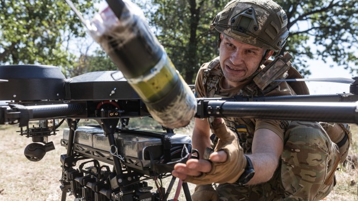 A Ukrainian soldier in camouflage uniform and helmet loads ammunition onto a large drone during field training.