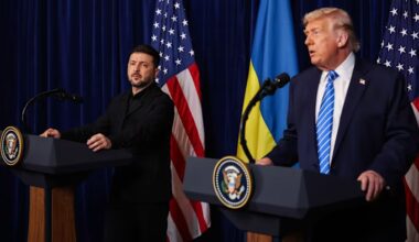Volodymyr Zelenskyy listens as Donald Trump speaks at podiums with US and Ukrainian flags behind them during a press conference.