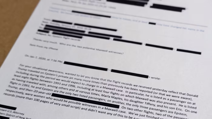 A printed email with numerous redactions is shown close up; the text discusses Jeffrey Epstein and related flight records