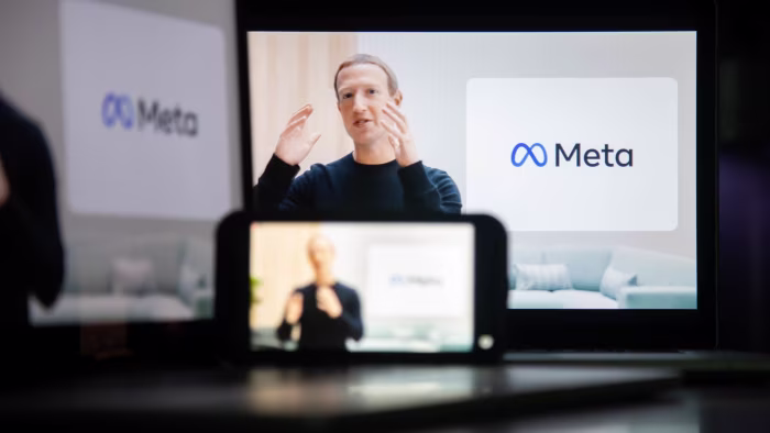 Mark Zuckerberg speaks during a virtual event announcing Facebook's rebranding as Meta, with the Meta logo visible on a screen behind him.