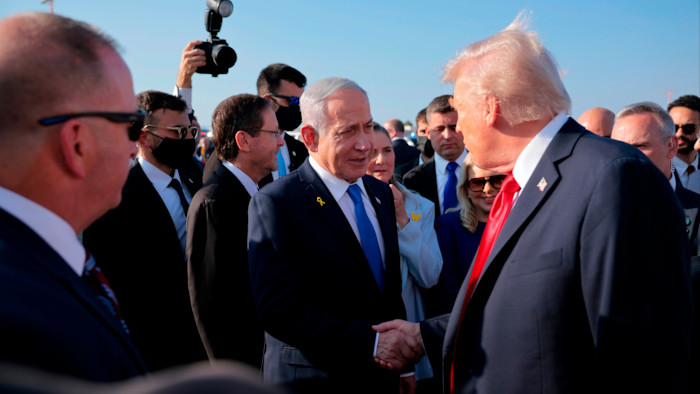 Donald Trump shakes hands with Benjamin Netanyahu while surrounded by officials and security personnel at an airport.