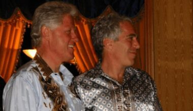 Bill Clinton stands beside Jeffrey Epstein, both smiling and wearing patterned shirts, in an indoor setting with gold drapes behind them. (Image supplied by the DoJ)