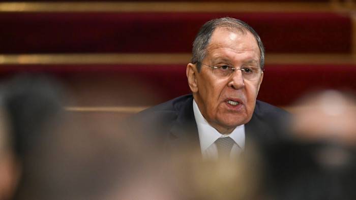 Sergey Lavrov speaks during a press conference, with blurred audience members in the foreground.