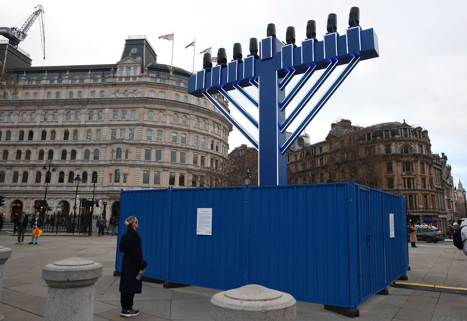 A woman stands in front of a large menorah with lights on top