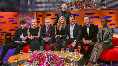Left to right: Owen Cooper, Carey Mulligan, Tim Key, Laura Dern, Will Arnett, Tom Hiddleston and Alson Limerick sit on a red curved sofa as Graham Norton stands behind them