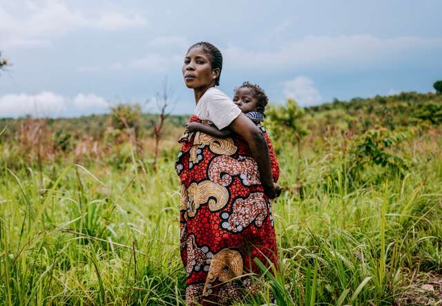 A mother holds her young child and walks through a field in the Democratic Republic of the Congo.