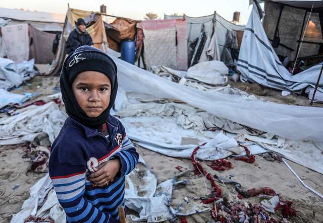 A young Palestinian boy stands in front of the ruins of a makeshift shelter in Gaza.