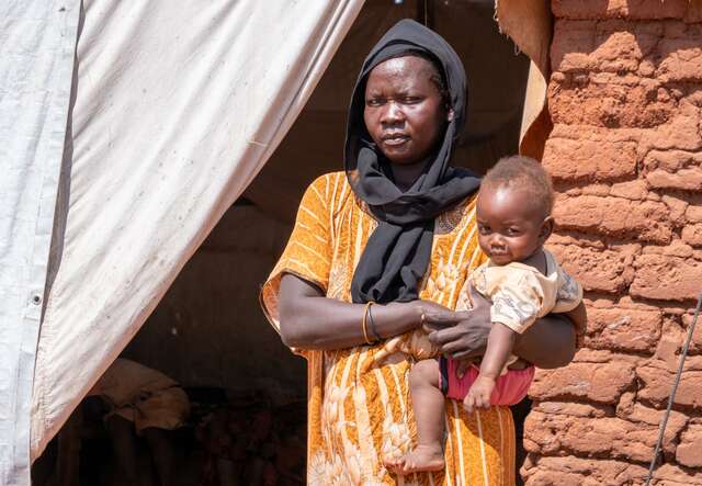 A mother holds her young daughter on the hip. They pose for a photo outside their home in South Sudan.