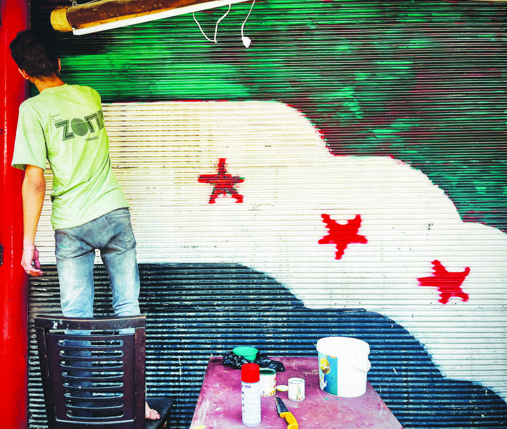 A man paints the Syrian opposition flag on a shopfront shutter in Damascus. Despite the government’s hold on the capital, signs of dissent still surface as residents adjust to political uncertainty after Bashar Assad’s departure 