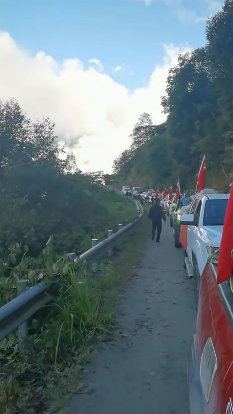 A line of cars and trucks flying Chinese flags and propaganda banners, transport Bangxin villagers to the Xigong settlement site, closer to the de facto China-India border.