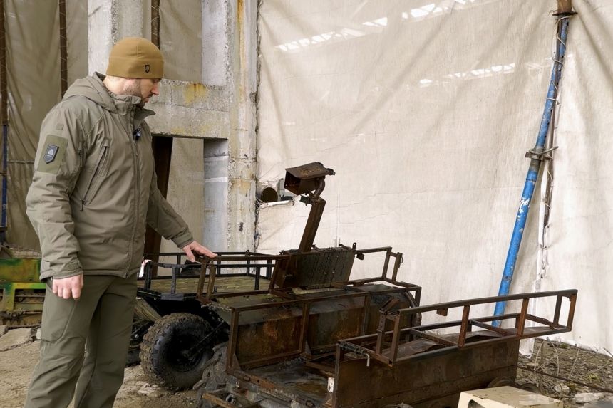 An instructor, known as Stark, points to a land drone that was burnt in action.