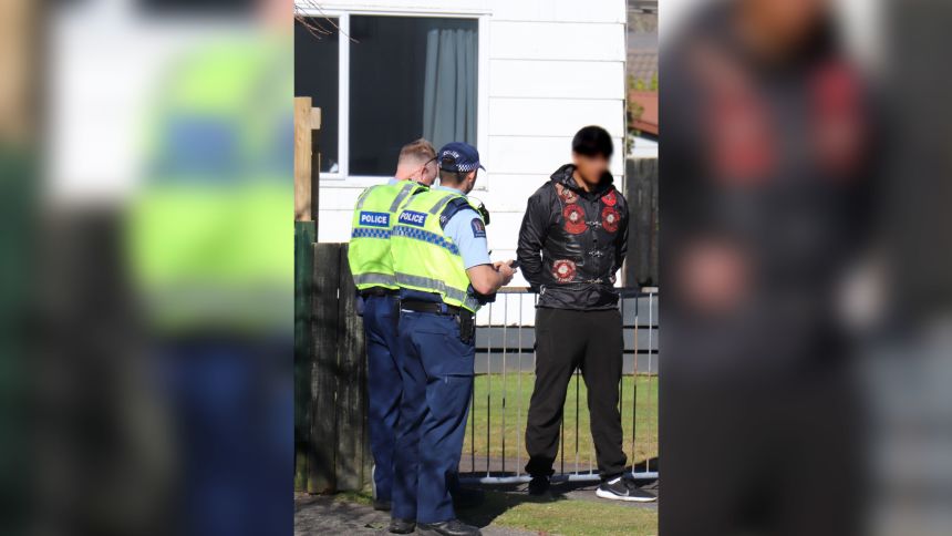 Police officers speak to a Mongrel Mob member wearing his patch in Rotorua around a funeral attended by a large number of gang members in August 2025.