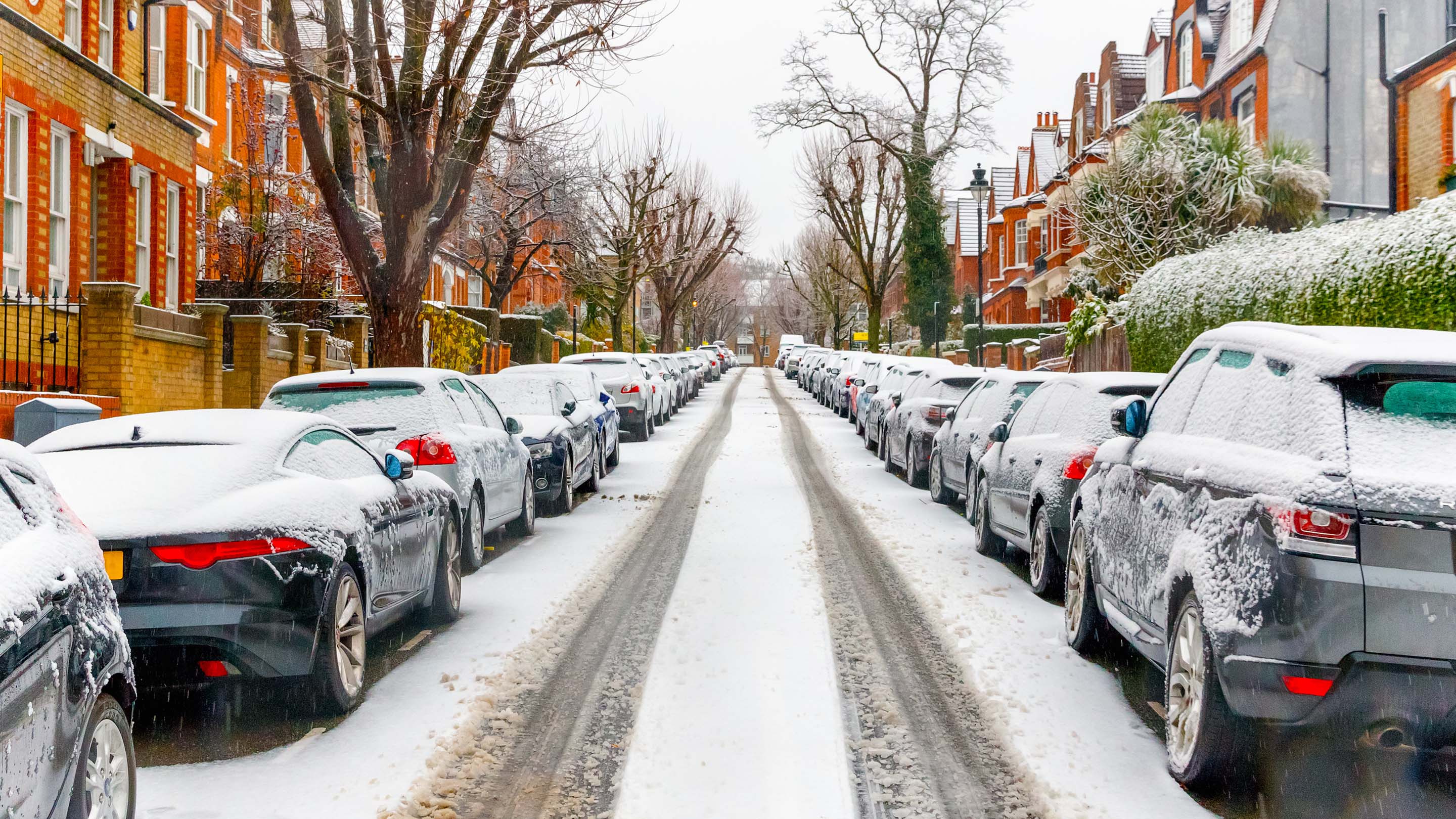 Street covered in snow with housing on either side and cars parked on both sides
