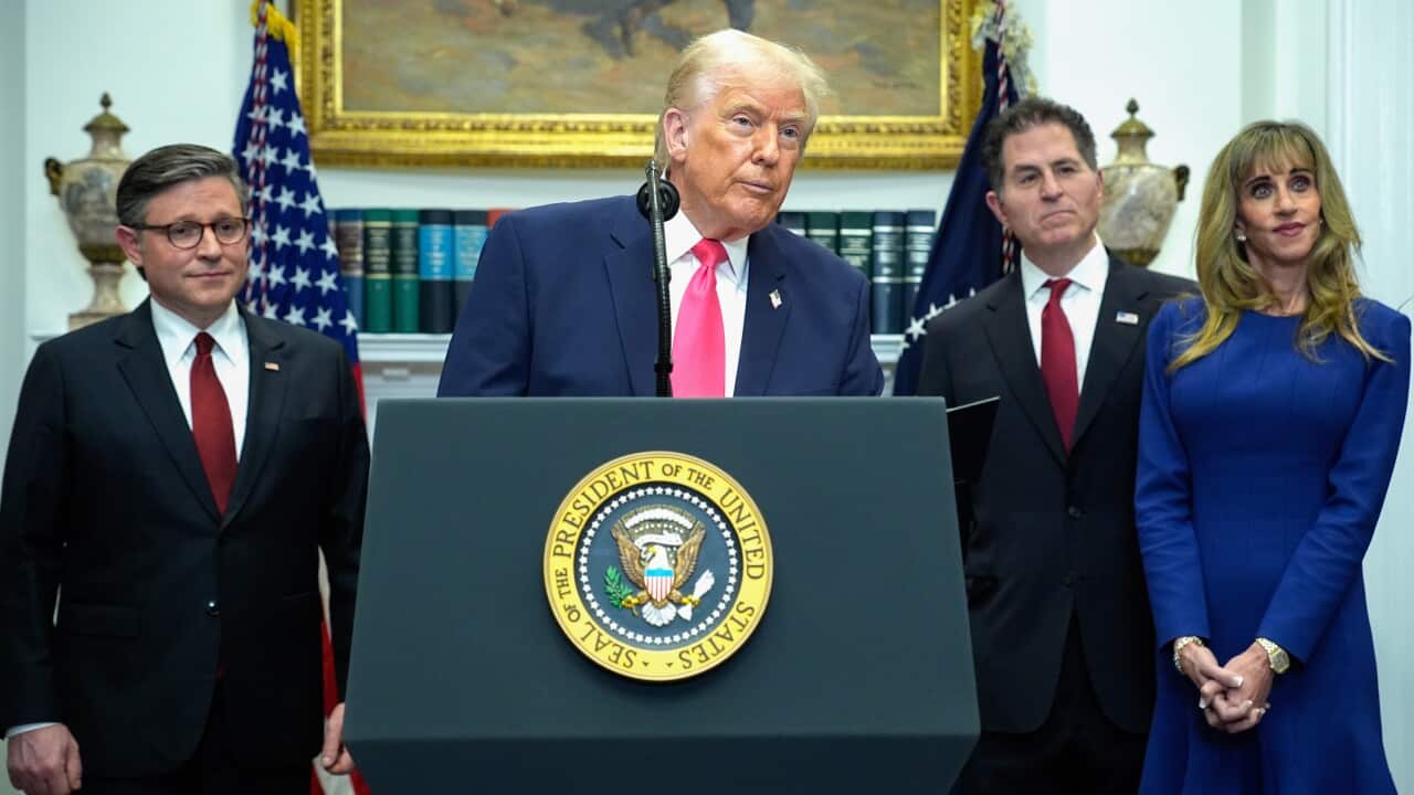 Donald Trump speaks at a podium inside the White House, with two men and a woman standing next to him.