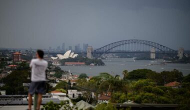 A man standing on a hill that overlooks a rainy Sydney Harbour.