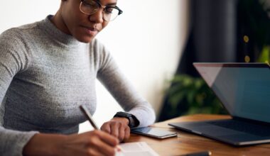 Investor writing in planner in front of laptop.