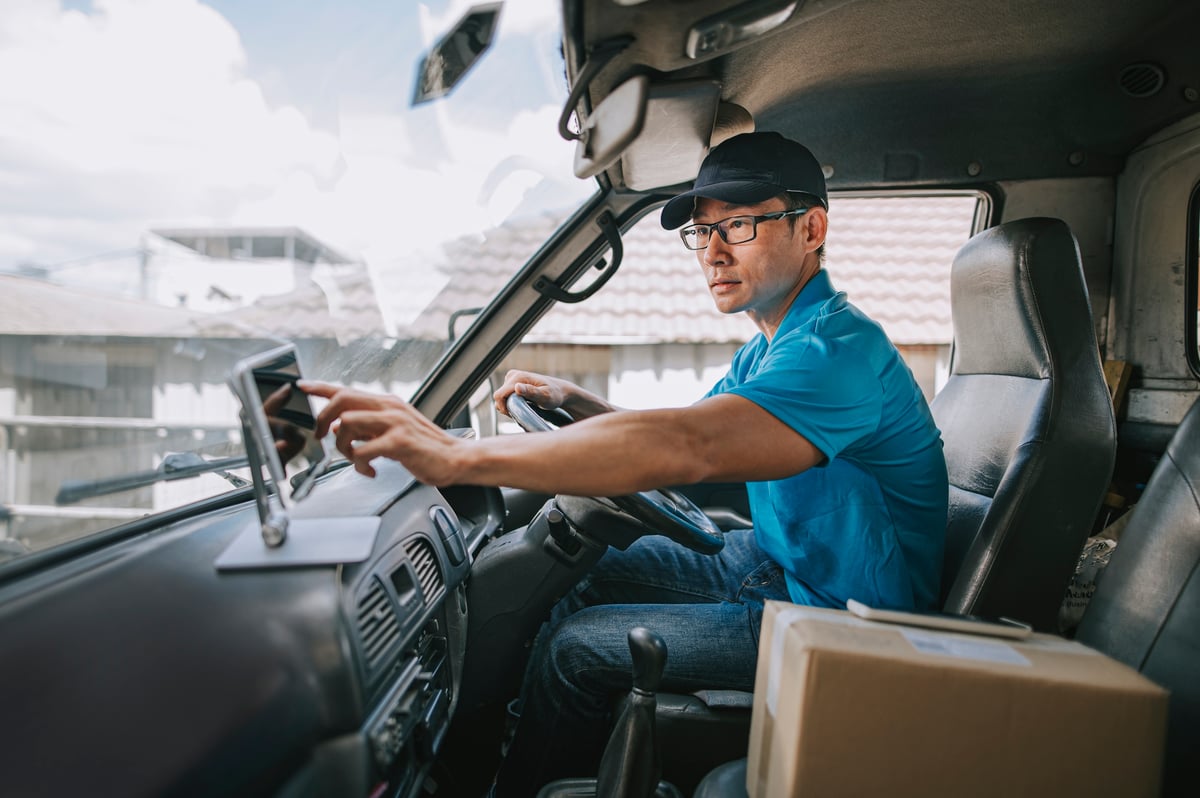 A delivery driver touching a dashboard in his delivery truck with a packaged box in his passenger seat.