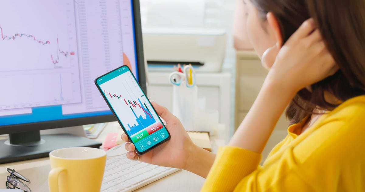 A person looking at crypto price targets on their phone and computer monitor.