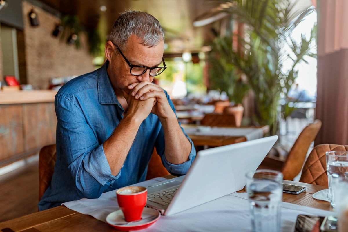 Investor with hands clasped looking at laptop screen.