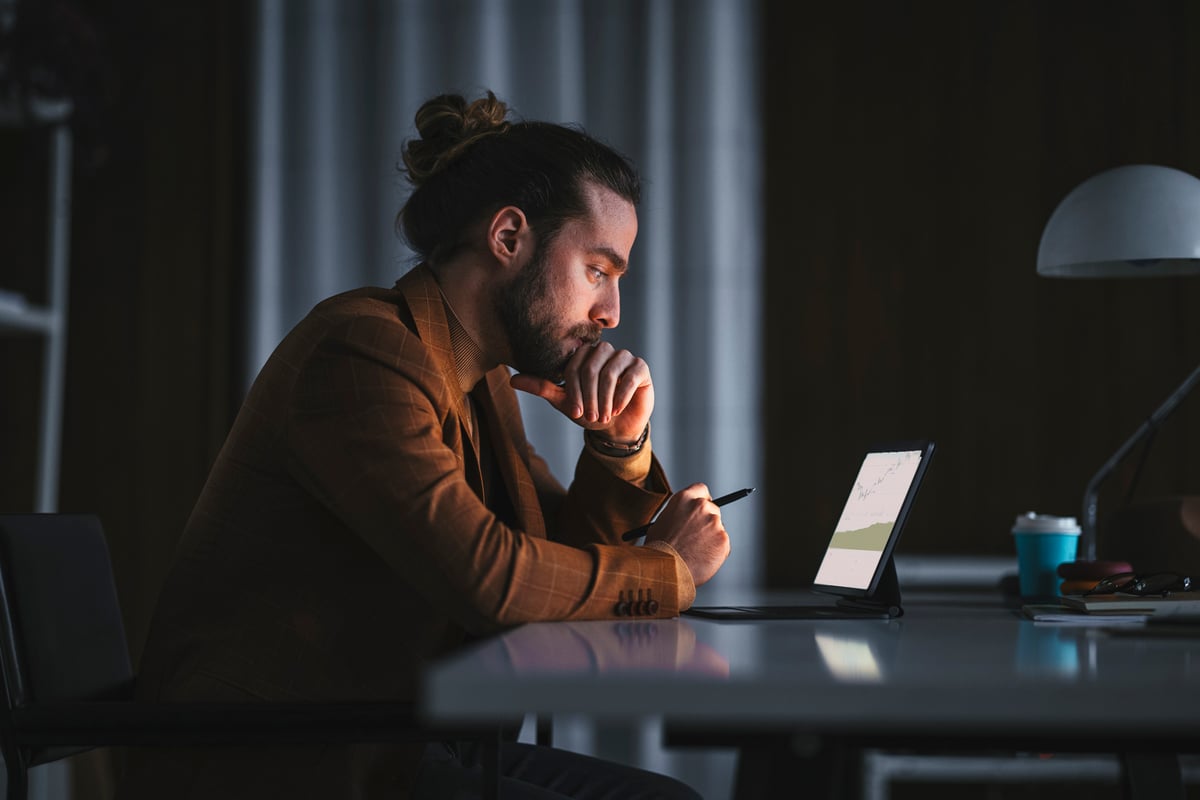 An investor looks at something on a tablet in a darkened office.