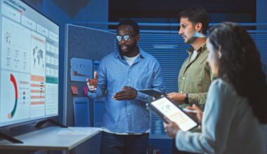 A team of professionals is discussing data dashboards on a large screen.