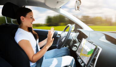 A driver in a moving car with both hands raised away from the steering wheel.