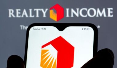 Realty Income logo on a phone with the company name and logo on a wall in the background.