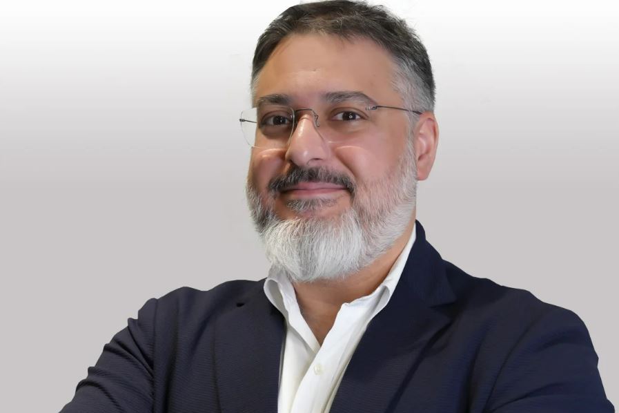 Headshot of Yaser Jabbar, a man with a gray beard and glasses, smiling with his arms crossed.
