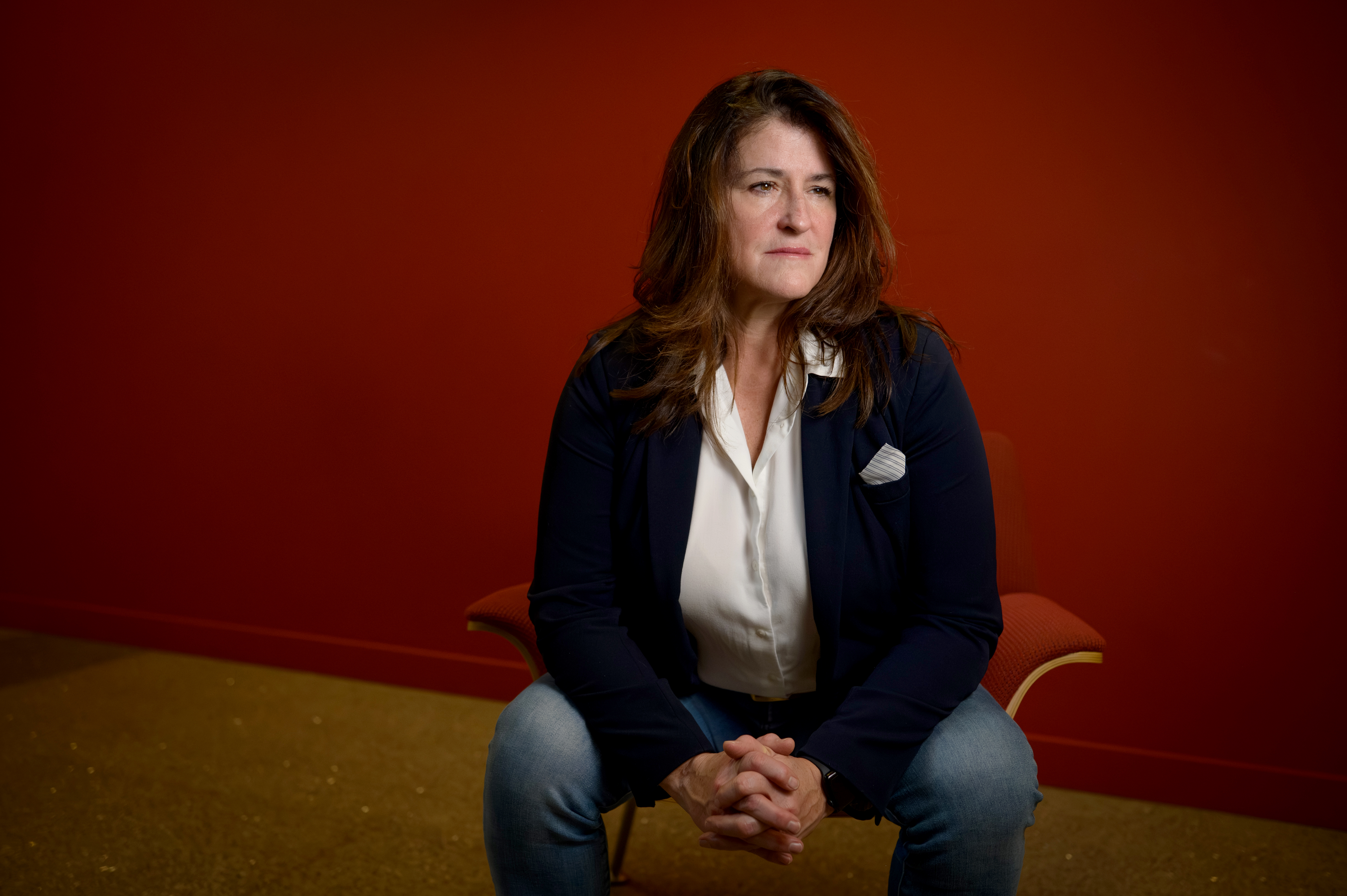 Dr. Theresa Vescio, a scholar of sexism, sits in a hallway against a red wall.