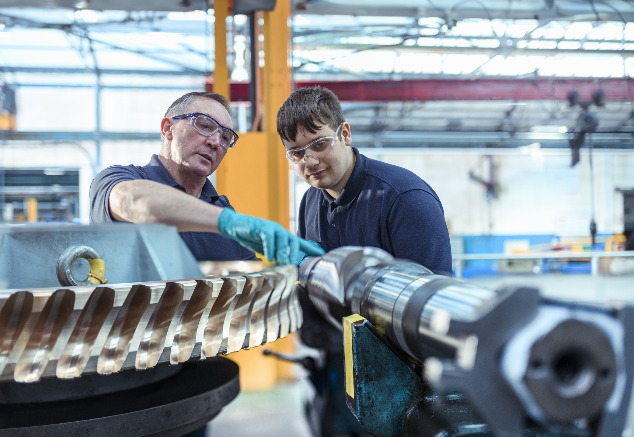 An older engineer mentoring an apprentice with worm gears in an engineering factory.