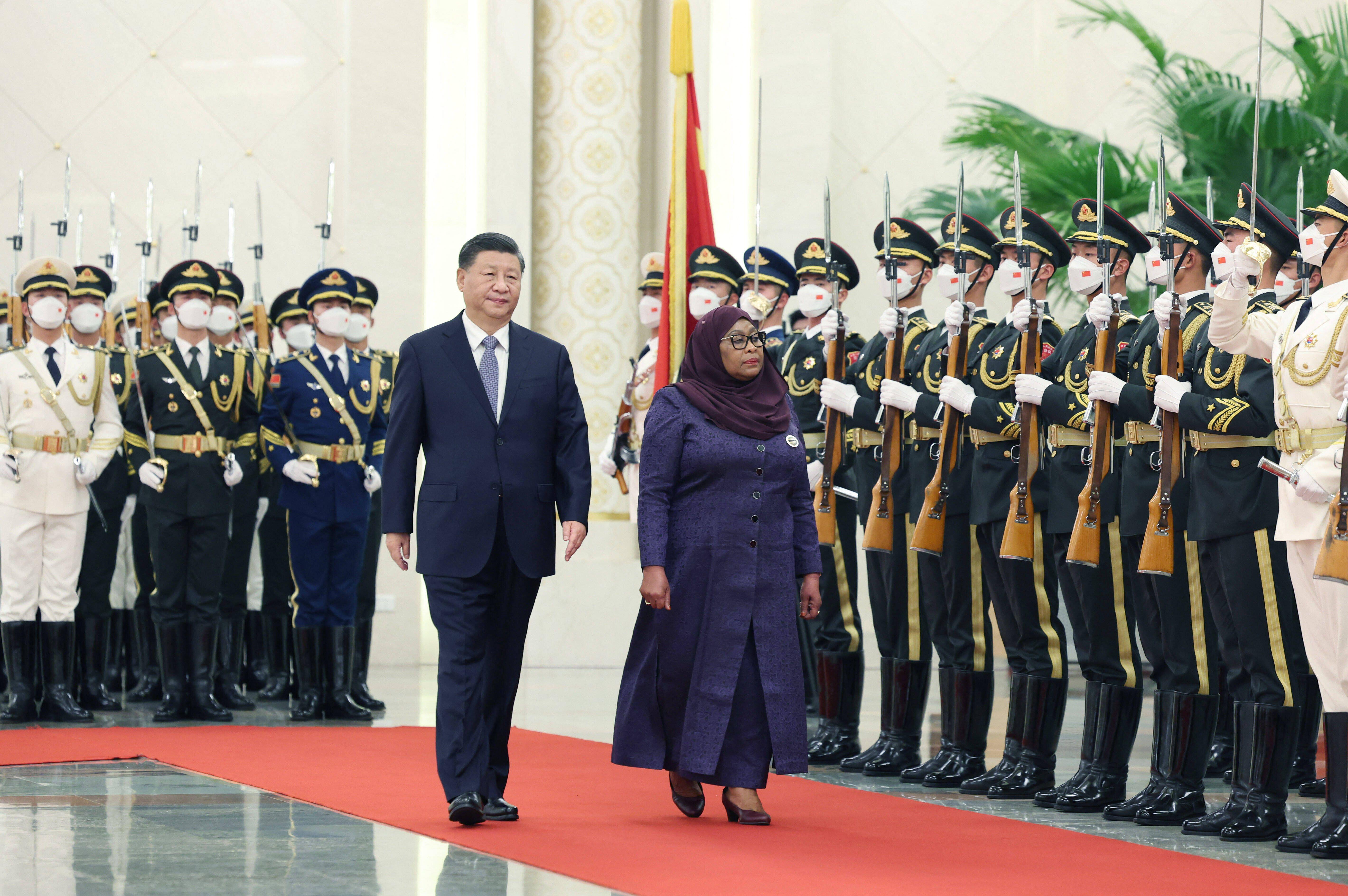 Chinese President Xi Jinping and Tanzanian President Samia Suluhu Hassan walk on a red carpet during a welcoming ceremony.