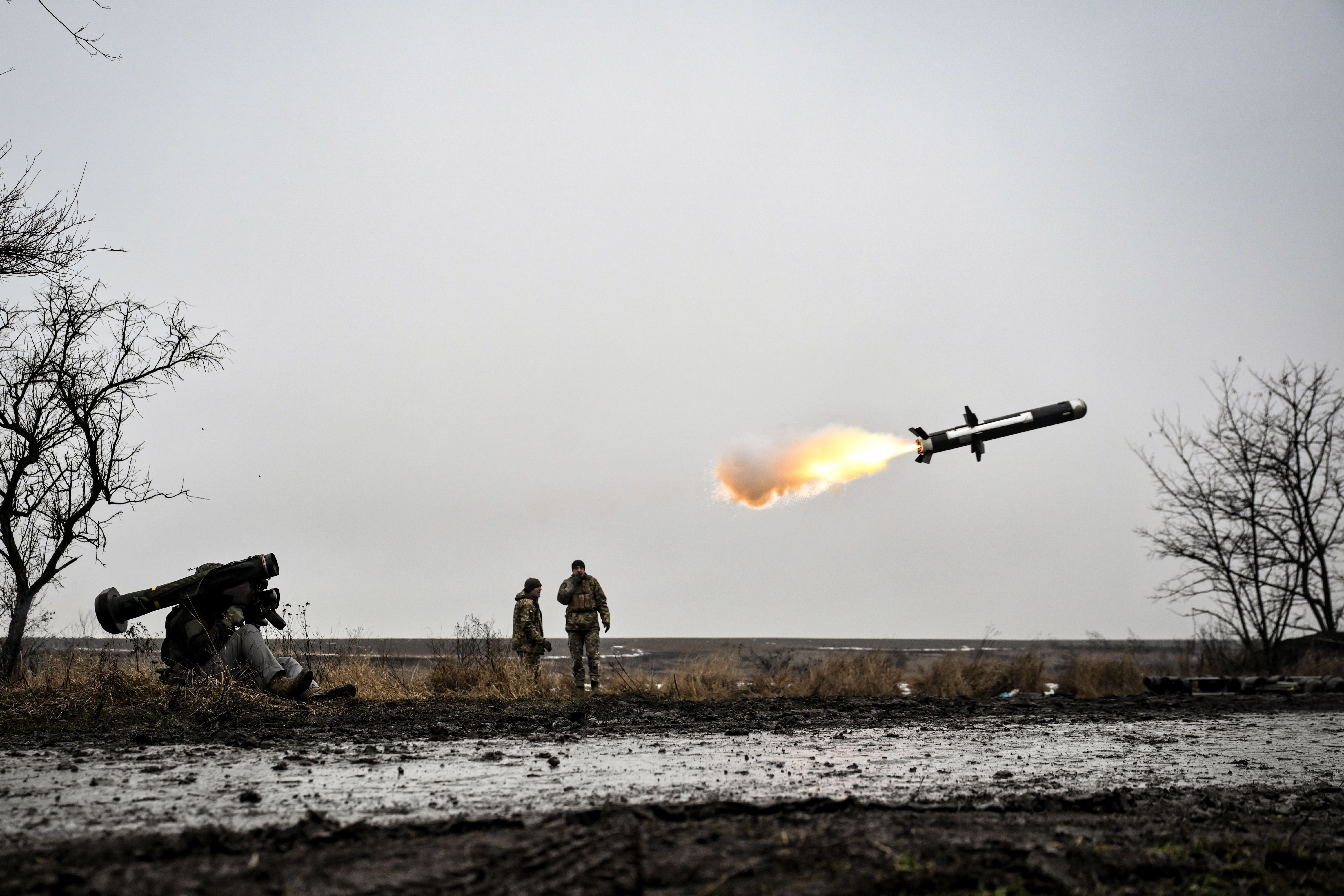 A soldier fires a Javelin anti-tank missile as two other soldiers look on from a muddy field.