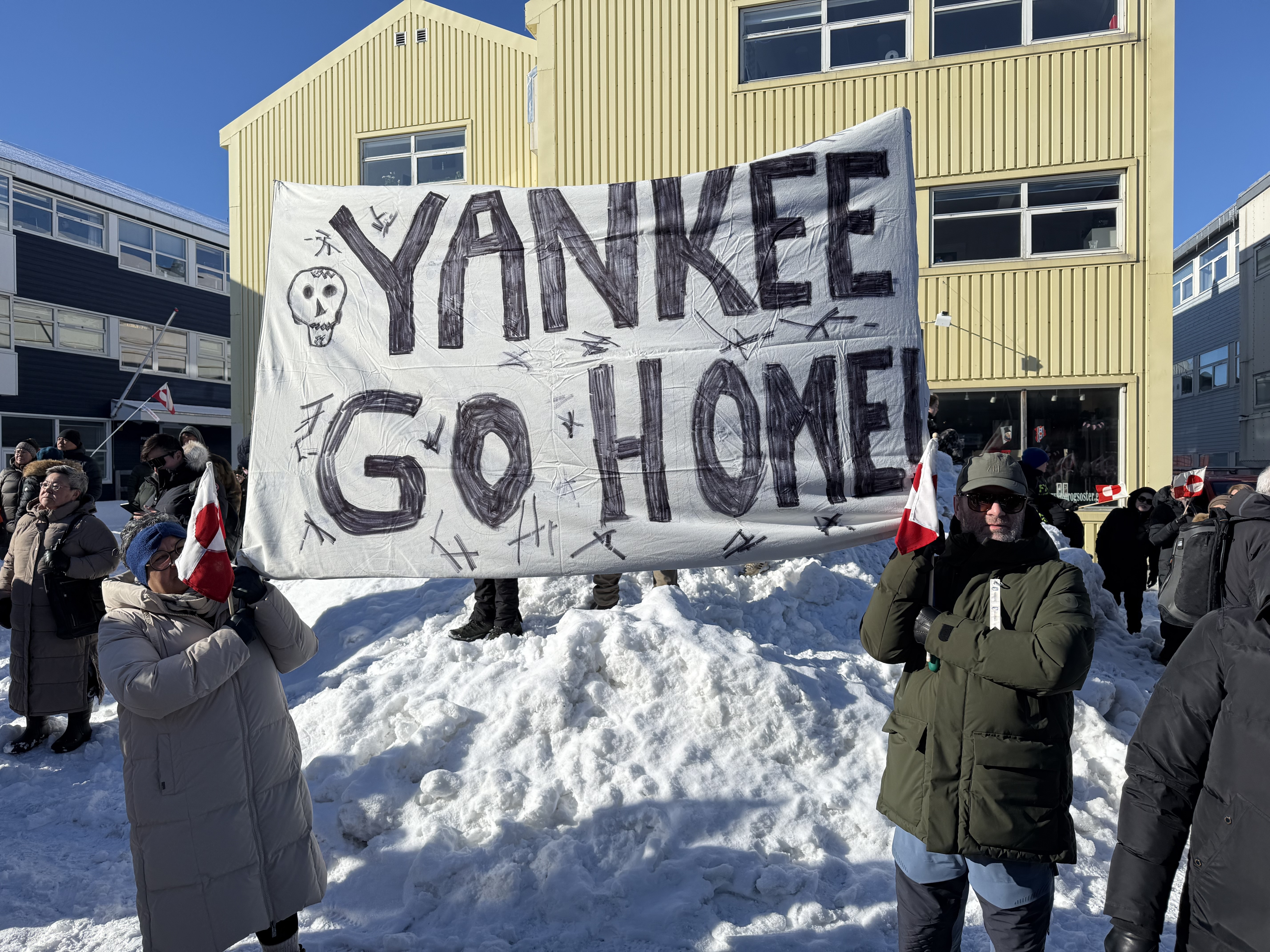Greenlanders protest US annexation bid, holding a "Yankee Go Home!" banner and Greenlandic flags.