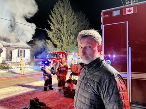 man stands next to house fire