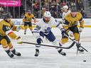 William Nylander of the Toronto Maple Leafs skates with the puck against Noah Hanifin (left) and Kaedan Korczak of the Vegas Golden Knights.