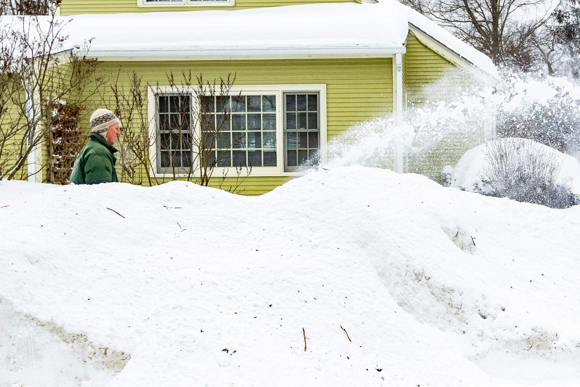 A man clears snow from the sidewalk with a snow blower behind a large snow bank on Thoreau Street in Concord in the morning following the first major snowstorm of the year. (Jesse Costa/WBUR)