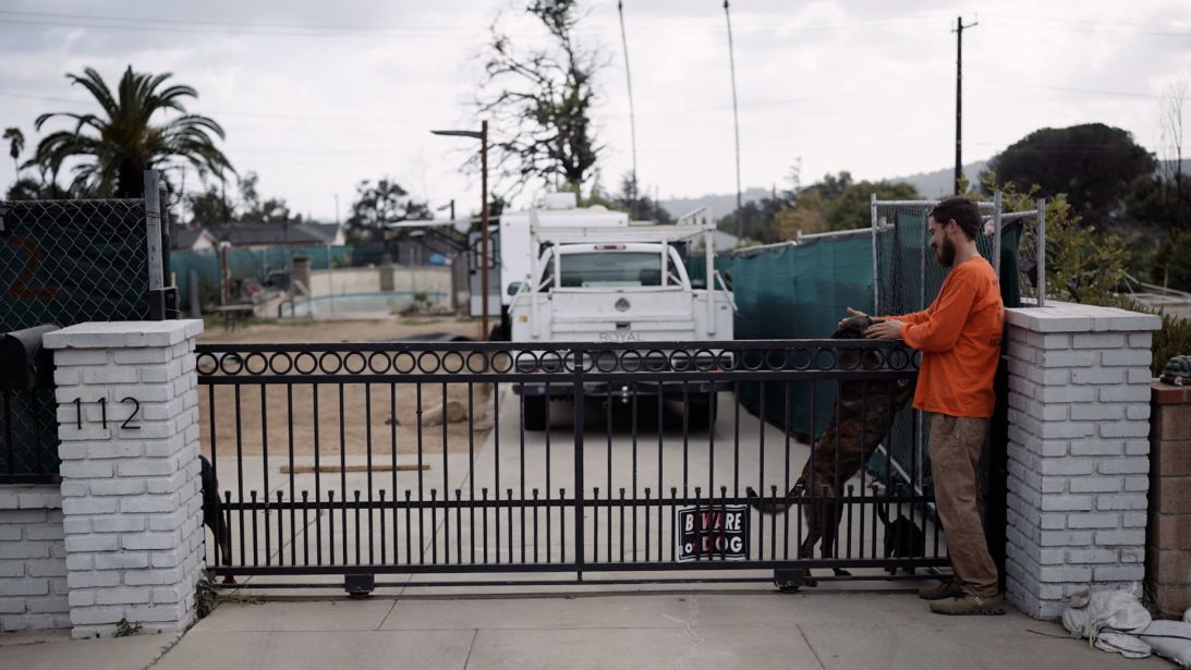 Robert Lara plays with his dog at his lot in Altadena, where he's moved into a trailer to oversee the rebuilding process.