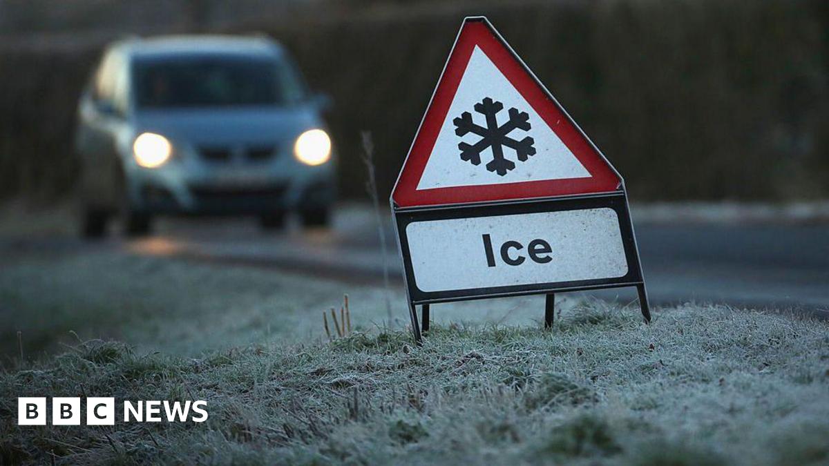 A road sign with a snowflake icon. There is a car driving on the road.