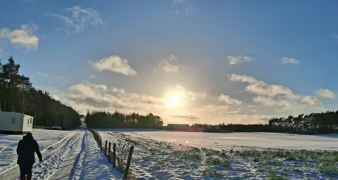 Eddie Middleton The sun setting over a snowy field. A person can be seen walking along a path next to the field